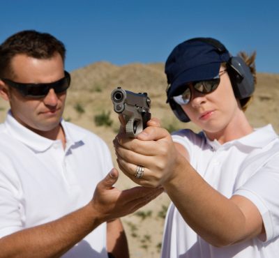 Instructor assisting woman aiming hand gun at firing range in desert